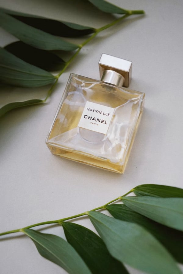 bottle of perfume laying down on white surface between two leaves